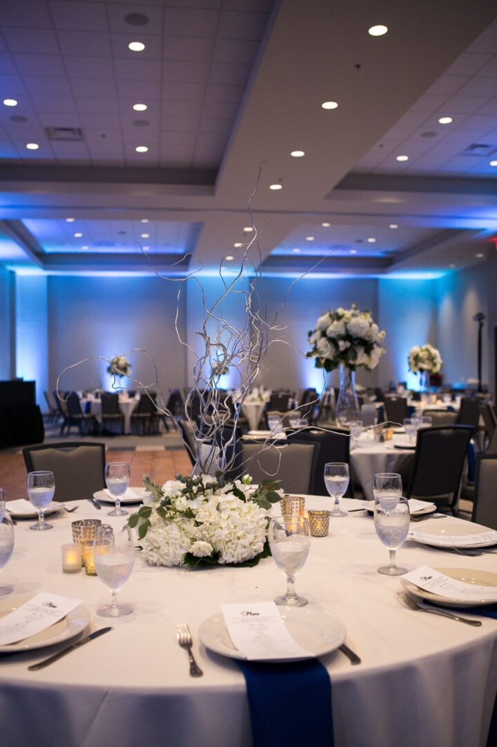 A banquet hall with tables and chairs, lights and flowers.