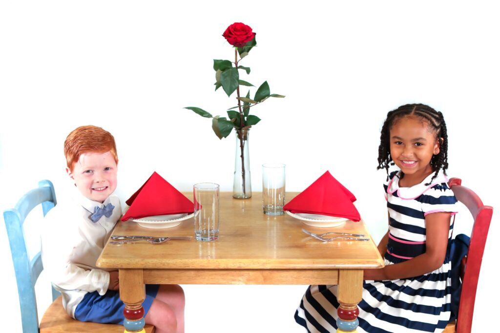 Two children sitting at a table with a rose on the top of it.