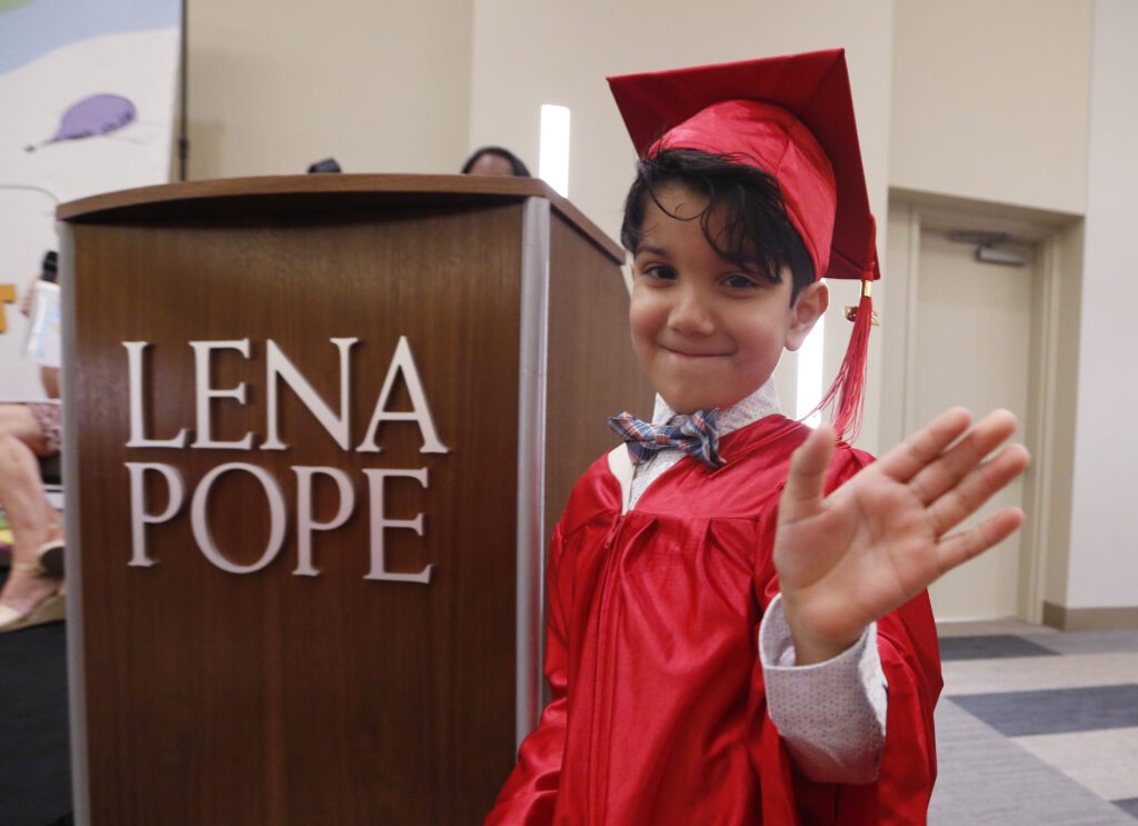 A young boy in red cap and gown waving.