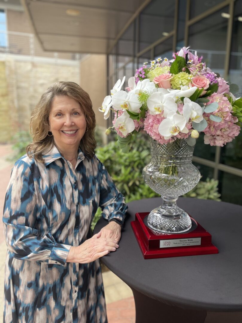 A woman standing next to a vase of flowers.