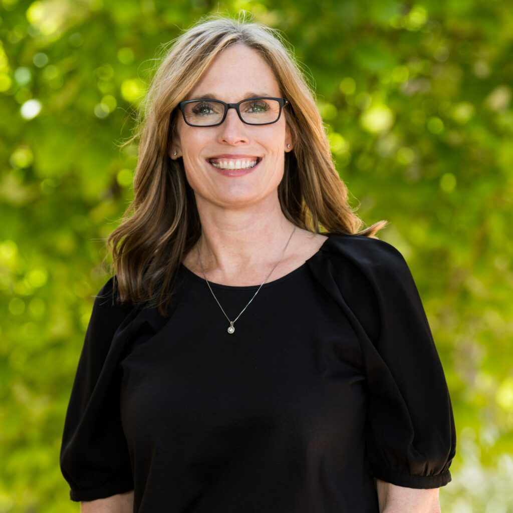 A woman in black shirt and glasses smiling for the camera.