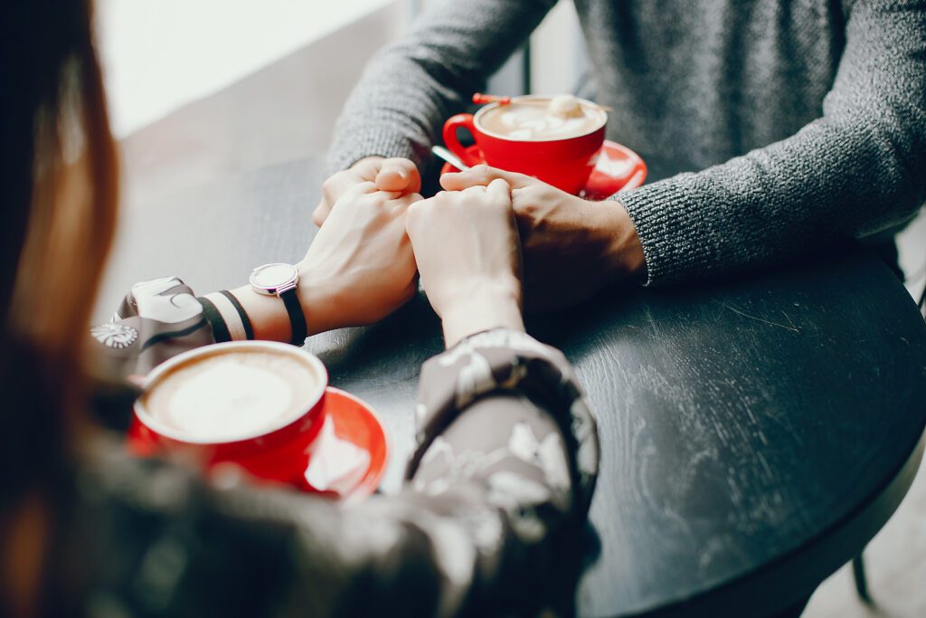 Two people holding hands over a table with cups of coffee.