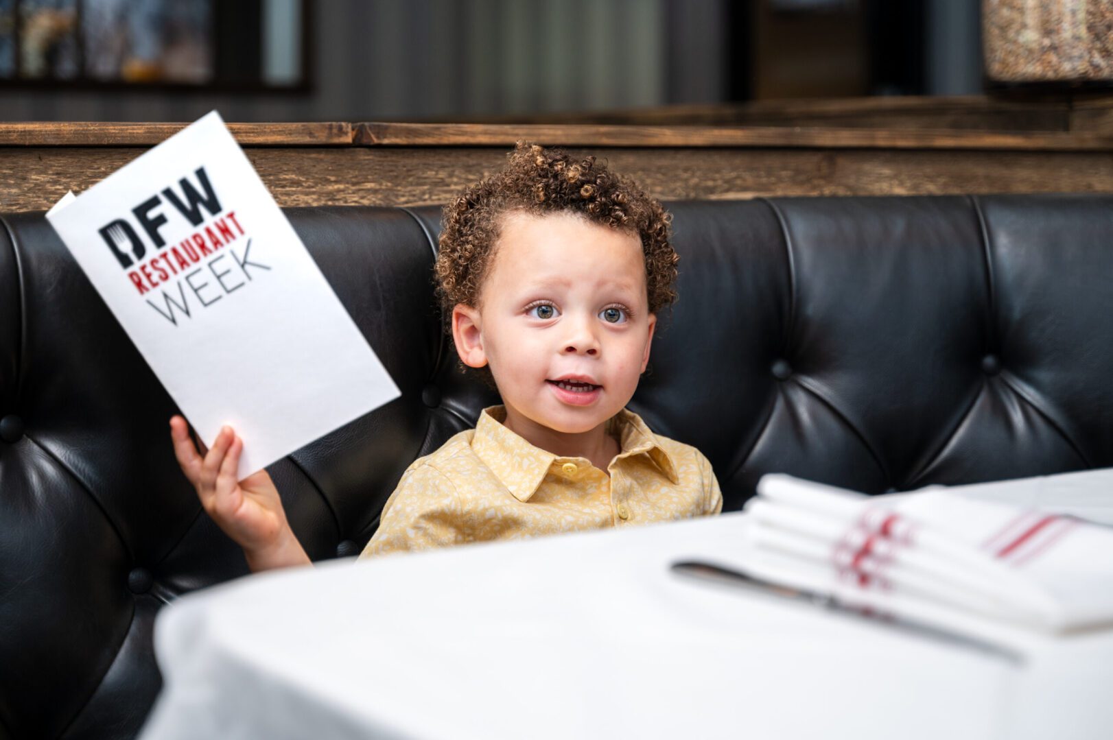 A young boy holding up a paper while sitting at the table.