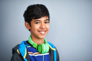 young boy with headphone and backpack smiling at camera